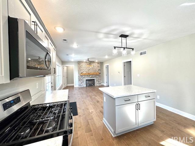 kitchen with light wood finished floors, visible vents, appliances with stainless steel finishes, and a stone fireplace