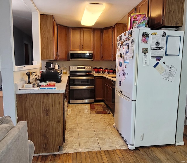 kitchen with light tile patterned floors, stainless steel appliances, brown cabinets, and light countertops