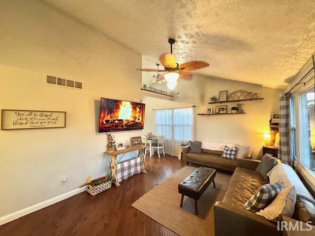 living room featuring visible vents, lofted ceiling, a wealth of natural light, wood finished floors, and a textured ceiling