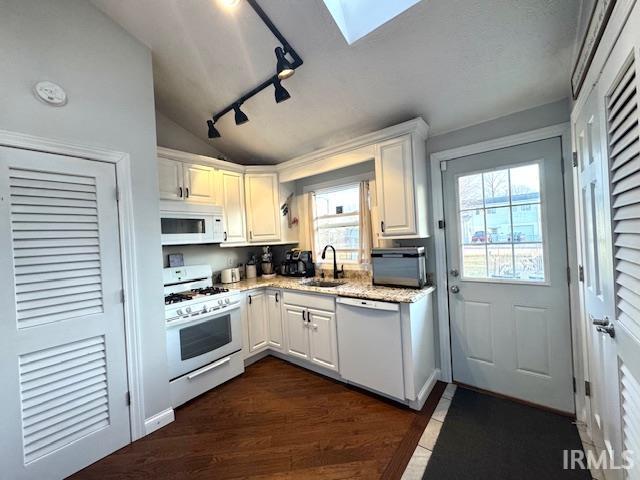 kitchen with dark wood-type flooring, vaulted ceiling with skylight, white cabinets, white appliances, and a sink