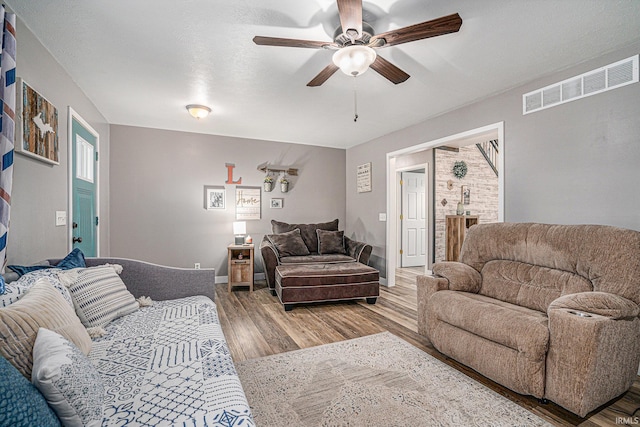 living room with ceiling fan, visible vents, a textured ceiling, and wood finished floors