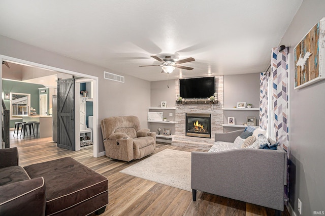 living room featuring visible vents, a barn door, a fireplace, wood finished floors, and a ceiling fan