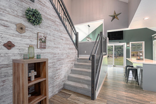 staircase featuring wood finished floors, a towering ceiling, and an accent wall