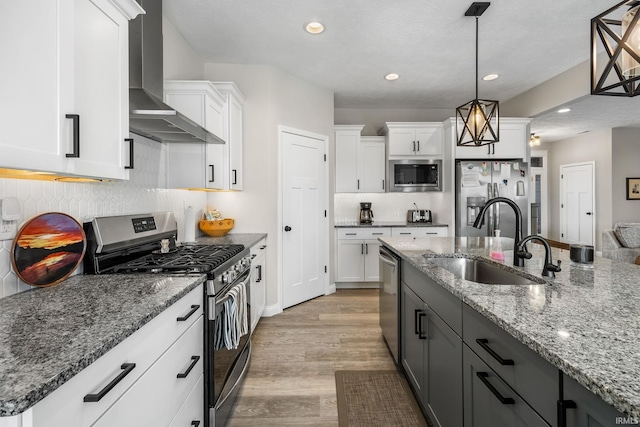 kitchen featuring a sink, white cabinets, light wood-style floors, appliances with stainless steel finishes, and wall chimney range hood