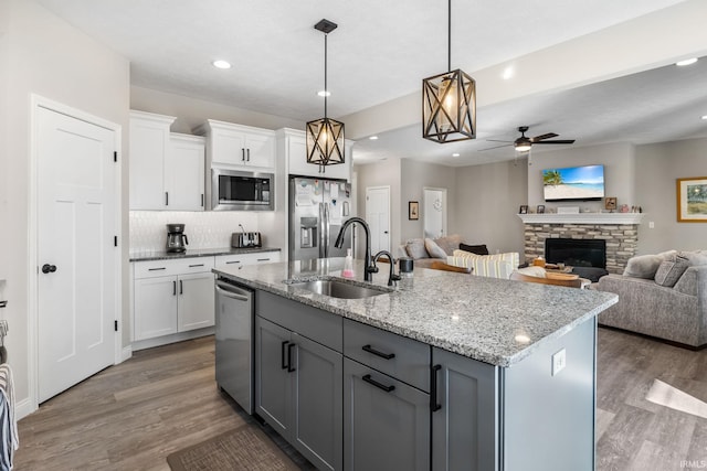 kitchen with a sink, stainless steel appliances, light wood-style floors, and a stone fireplace