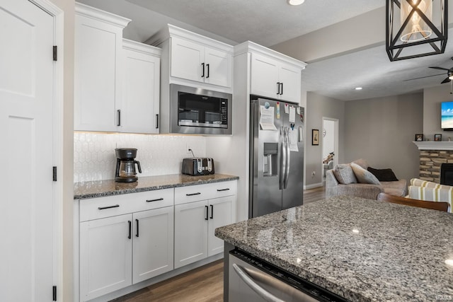 kitchen with open floor plan, dark stone countertops, appliances with stainless steel finishes, wood finished floors, and white cabinets