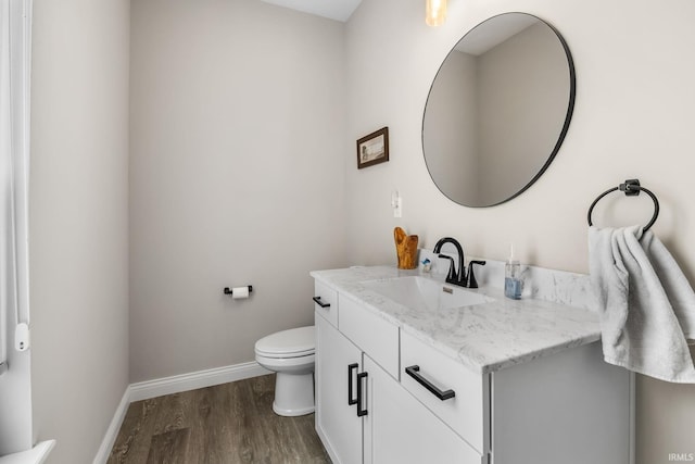 bathroom with toilet, vanity, baseboards, and wood finished floors