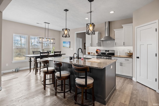 kitchen featuring visible vents, stainless steel range with gas stovetop, a sink, wall chimney range hood, and tasteful backsplash