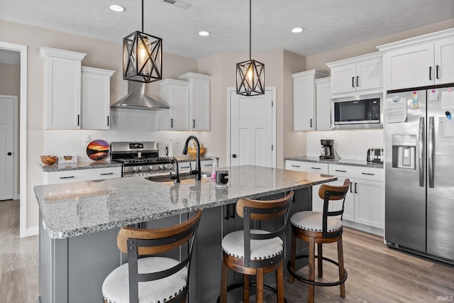 kitchen with a center island with sink, a sink, appliances with stainless steel finishes, white cabinetry, and light wood-type flooring