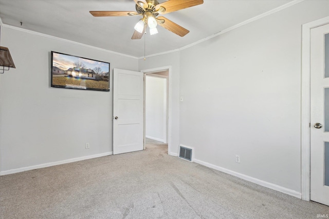 carpeted empty room with a ceiling fan, crown molding, baseboards, and visible vents