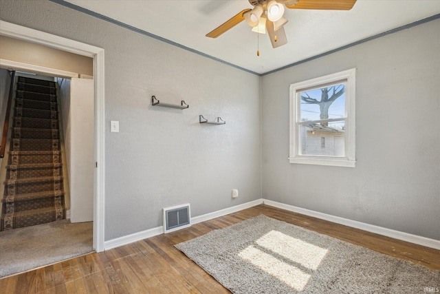 spare room with visible vents, wood-type flooring, baseboards, ceiling fan, and stairs