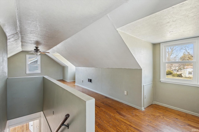 additional living space featuring lofted ceiling, wood finished floors, baseboards, and a textured ceiling