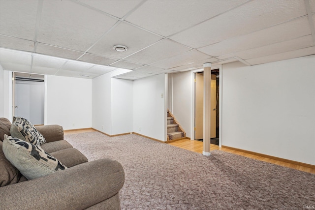 carpeted living area with stairway, baseboards, and a drop ceiling