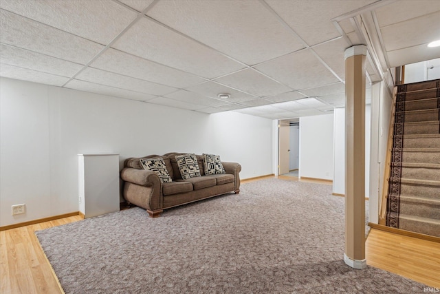 living room with a drop ceiling, baseboards, wood finished floors, and stairs