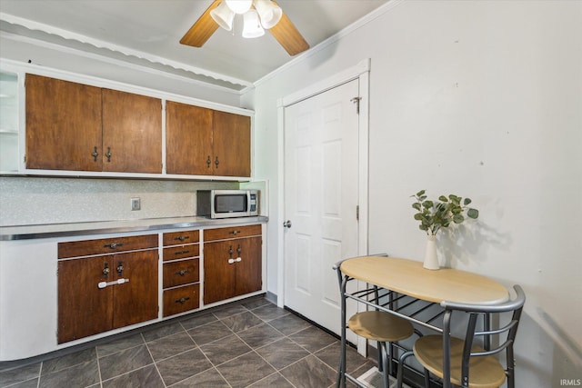 kitchen featuring ornamental molding, a ceiling fan, stainless steel microwave, tasteful backsplash, and light countertops