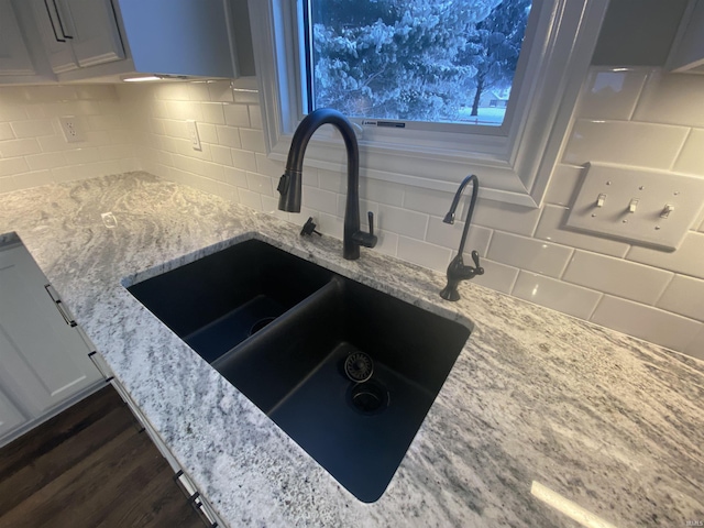 details featuring a sink, decorative backsplash, light stone countertops, and dark wood-style flooring