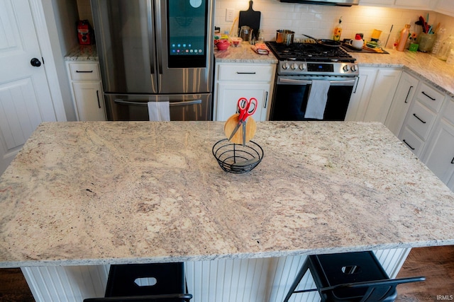 kitchen featuring tasteful backsplash, a kitchen island, light stone counters, white cabinets, and stainless steel appliances