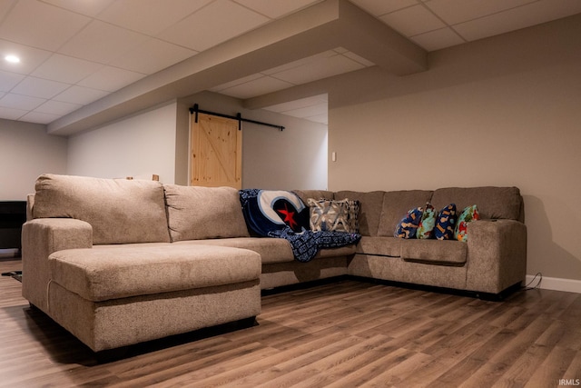 living area with a drop ceiling, baseboards, a barn door, and wood finished floors