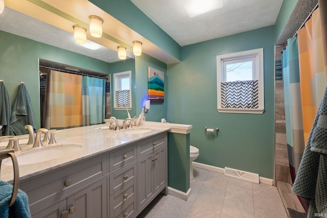 bathroom with a textured ceiling, toilet, visible vents, and a sink