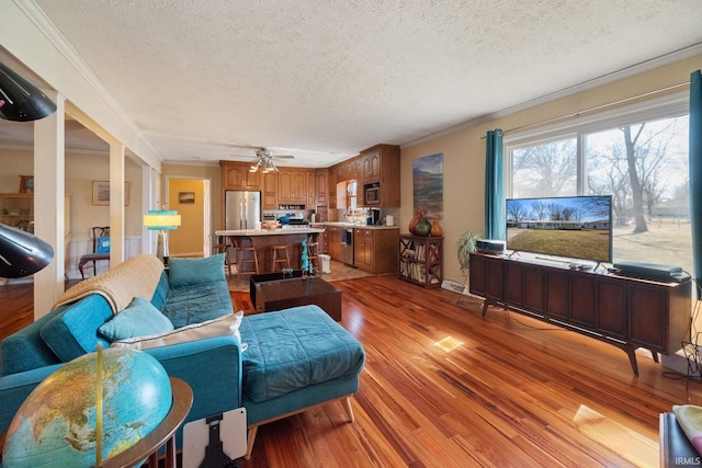 living area with a textured ceiling, light wood-type flooring, and crown molding