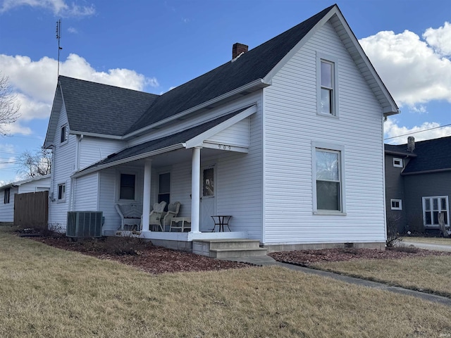 view of front facade with a porch, central AC, a front yard, roof with shingles, and a chimney