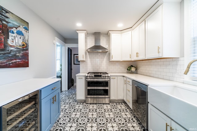 kitchen with a sink, wall chimney range hood, stainless steel appliances, wine cooler, and light countertops