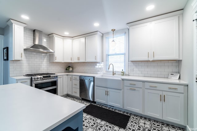 kitchen featuring a sink, light countertops, appliances with stainless steel finishes, white cabinetry, and wall chimney exhaust hood