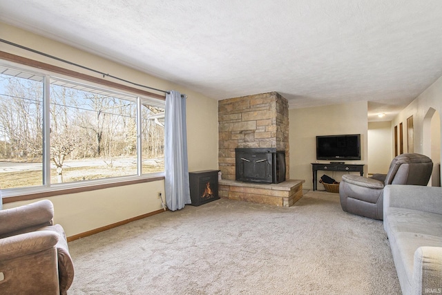 carpeted living area featuring a stone fireplace, baseboards, and a textured ceiling