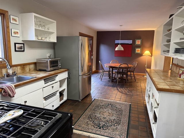 kitchen with a sink, tile countertops, freestanding refrigerator, and open shelves