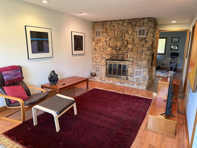 living room featuring visible vents, a stone fireplace, and hardwood / wood-style flooring