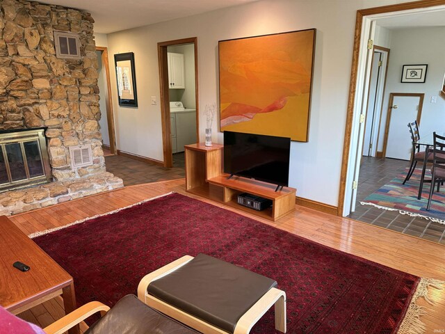 living room with a stone fireplace, washer / clothes dryer, wood finished floors, and visible vents