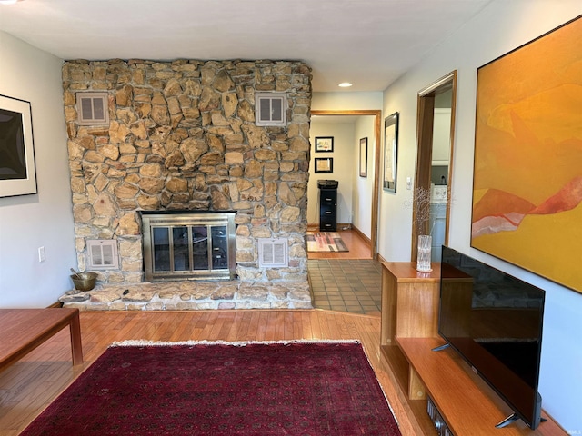 unfurnished living room with a stone fireplace, wood finished floors, and visible vents