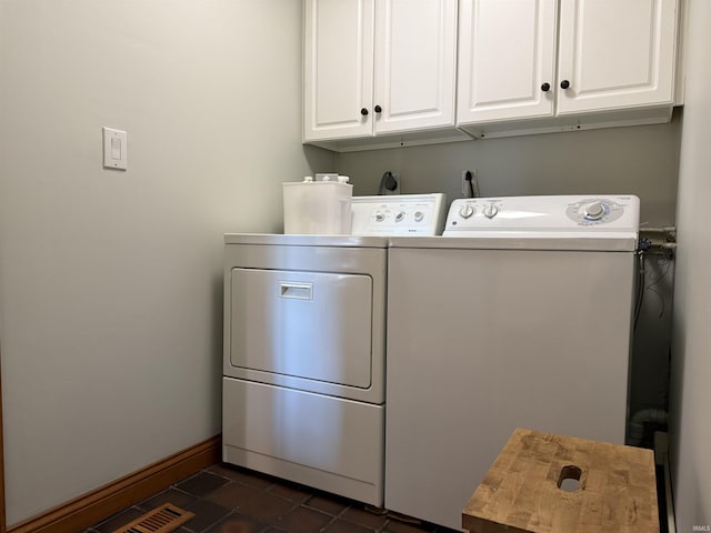 clothes washing area featuring baseboards, cabinet space, dark tile patterned floors, and washer and clothes dryer