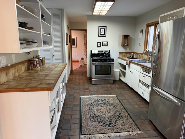 kitchen with a sink, open shelves, white cabinetry, appliances with stainless steel finishes, and tile counters