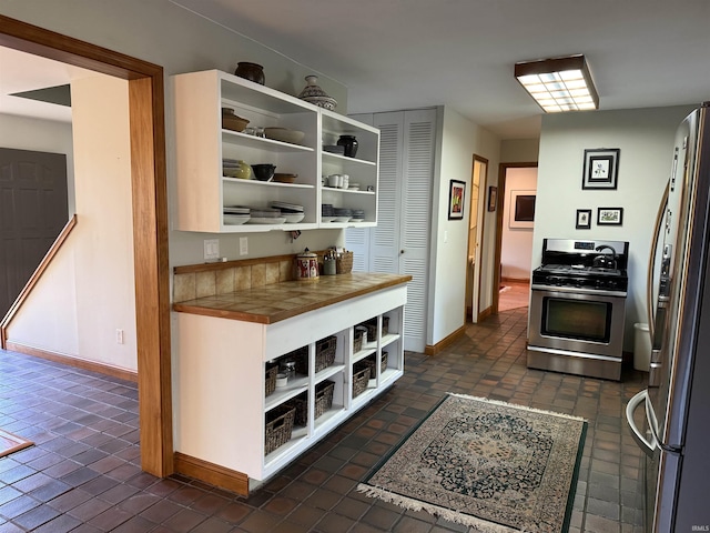 kitchen with open shelves, baseboards, appliances with stainless steel finishes, and tile countertops