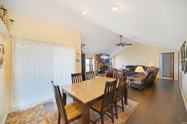 dining room featuring dark wood finished floors, vaulted ceiling, a ceiling fan, and a large fireplace