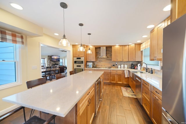 kitchen featuring a sink, wall chimney range hood, backsplash, appliances with stainless steel finishes, and light countertops