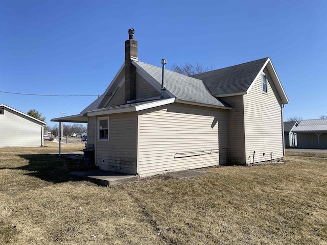 rear view of property with a carport, a yard, a chimney, and a shingled roof