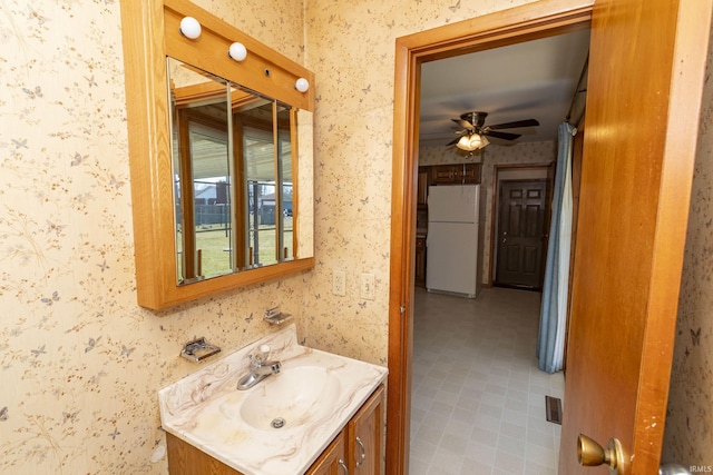 bathroom featuring a ceiling fan, vanity, and wallpapered walls