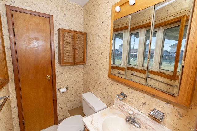 bathroom featuring toilet, a healthy amount of sunlight, vanity, and wallpapered walls