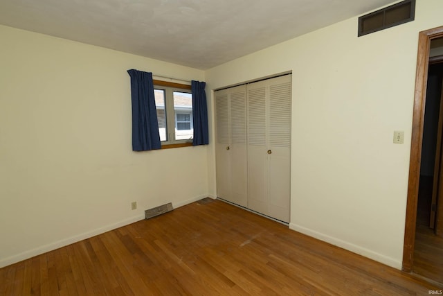 unfurnished bedroom with visible vents, baseboards, a closet, and hardwood / wood-style floors