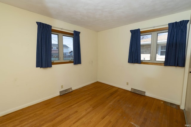 spare room featuring visible vents, baseboards, and hardwood / wood-style floors