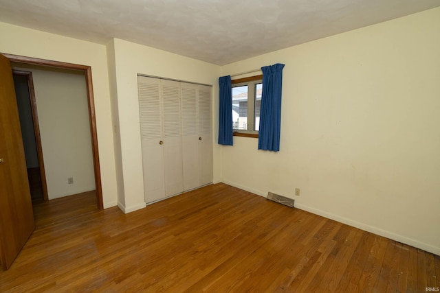 unfurnished bedroom featuring a closet, baseboards, visible vents, and wood finished floors