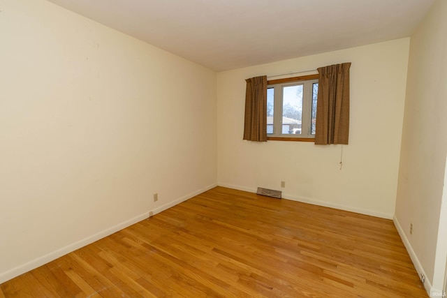 spare room featuring light wood-style floors, visible vents, and baseboards