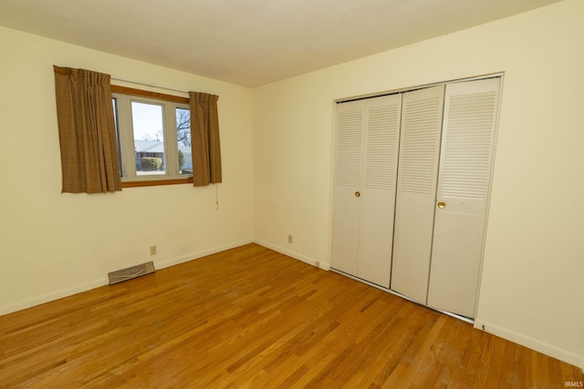 unfurnished bedroom featuring wood finished floors, visible vents, a closet, and baseboards