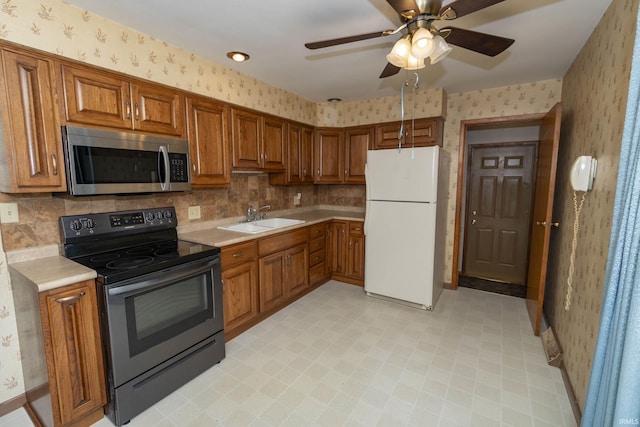 kitchen featuring brown cabinetry, wallpapered walls, a sink, stainless steel appliances, and light countertops