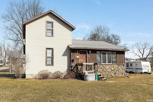 back of property featuring a shingled roof and a yard