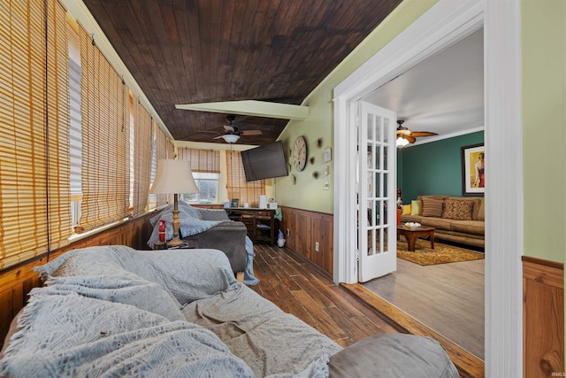 living area with wood ceiling, ornamental molding, wainscoting, wood finished floors, and a ceiling fan