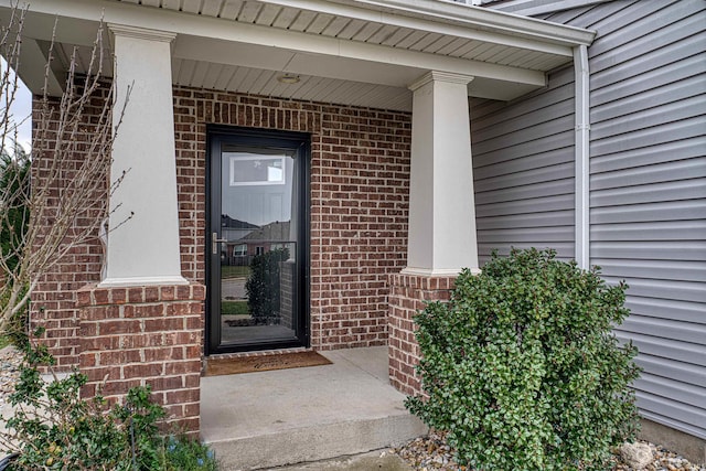 view of exterior entry featuring brick siding and covered porch