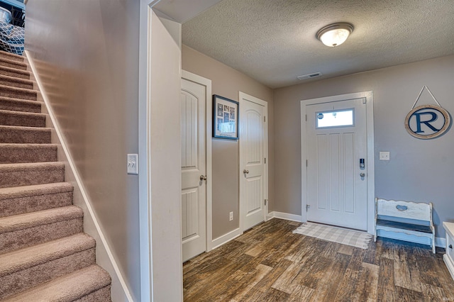 foyer entrance with stairway, baseboards, visible vents, dark wood finished floors, and a textured ceiling